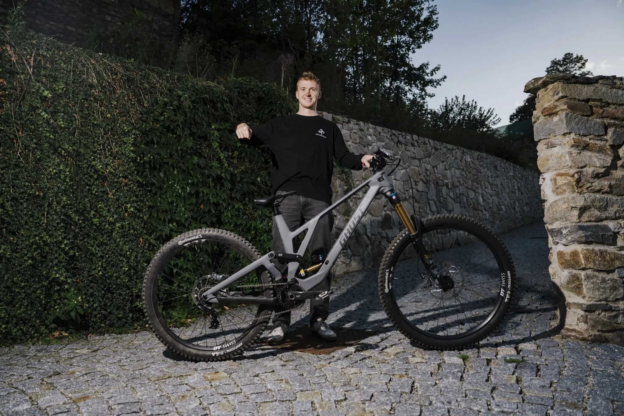 Tomáš Král stojí za novým kolem Ghost na dlážděné cestě u kamenné zdi